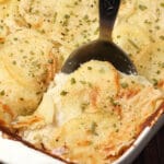 Vegan scalloped potatoes in a white dish with a serving spoon.