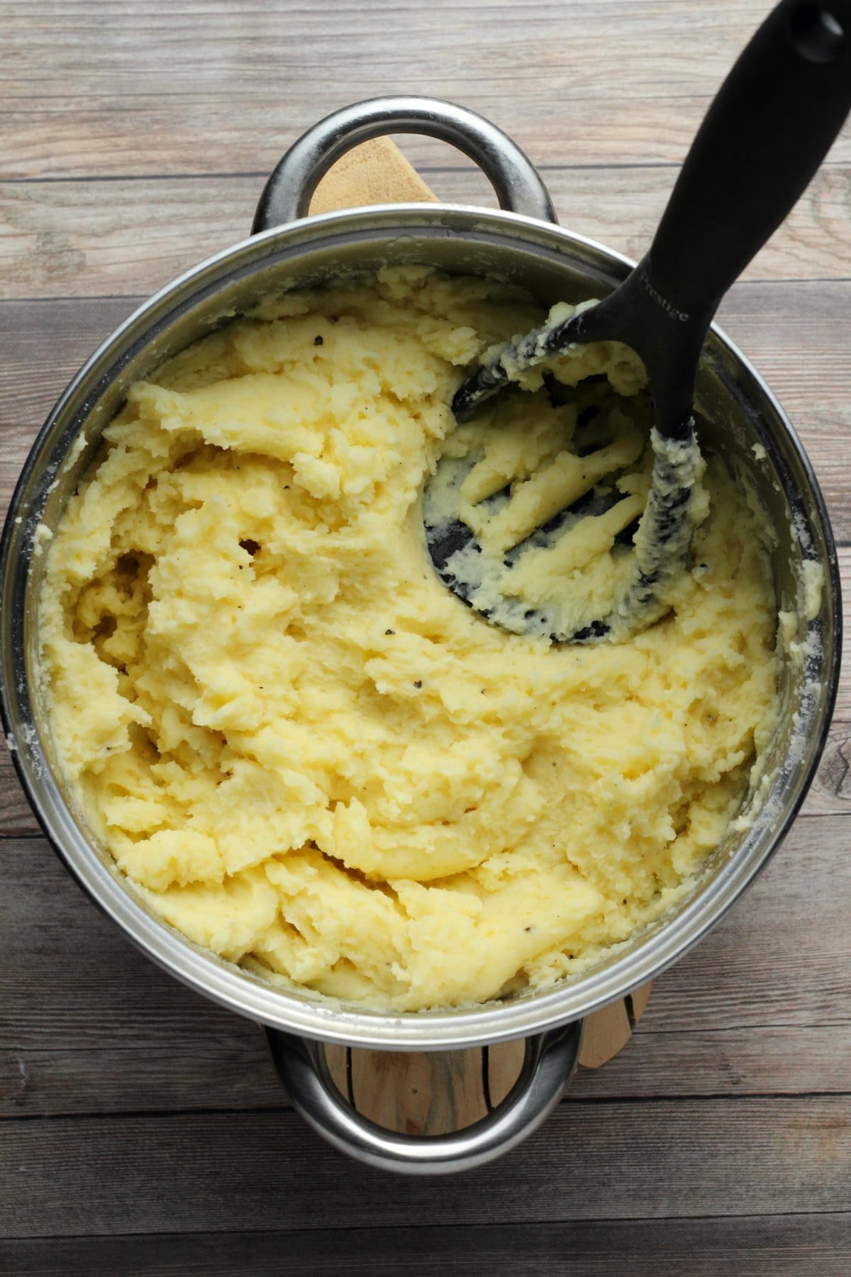 Vegan mashed potatoes in a pot with a potato masher.