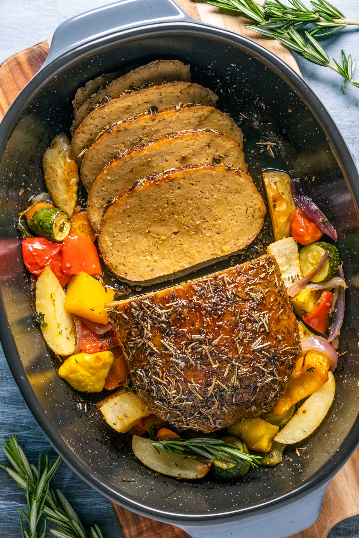 Sliced vegan turkey roast in a roasting pan with vegetables. 