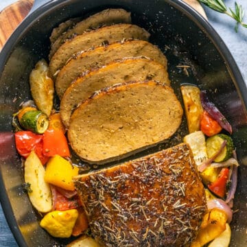 Vegan turkey roast with vegetables in a roasting dish.