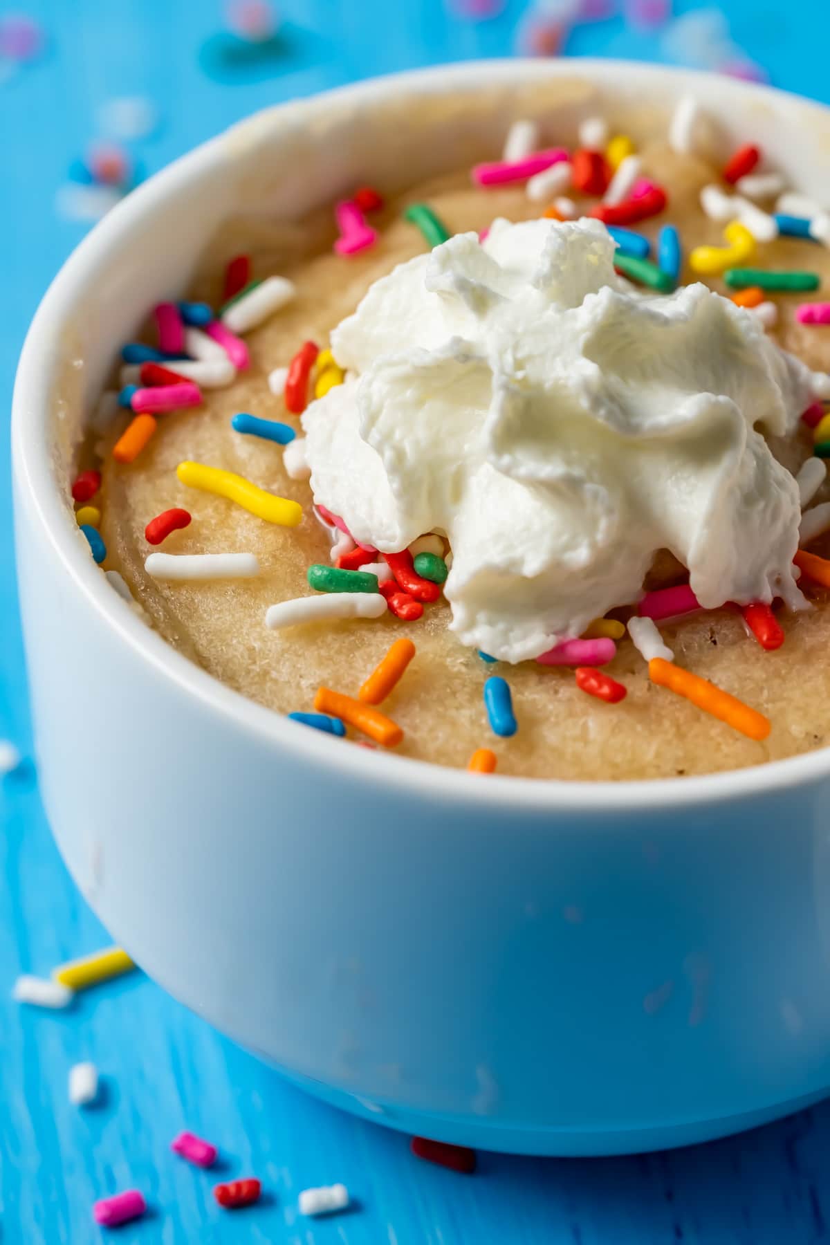 Vegan vanilla mug cake in a white mug topped with sprinkles and whipped cream. 