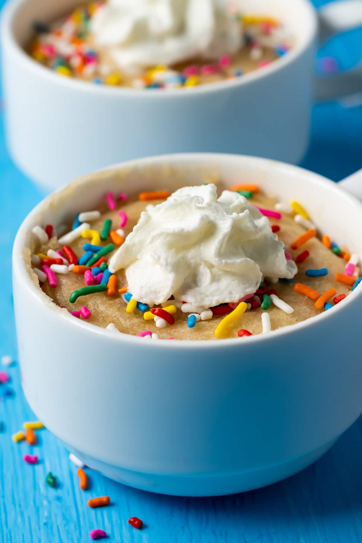 Vegan vanilla mug cake in a white mug topped with sprinkles and whipped cream.