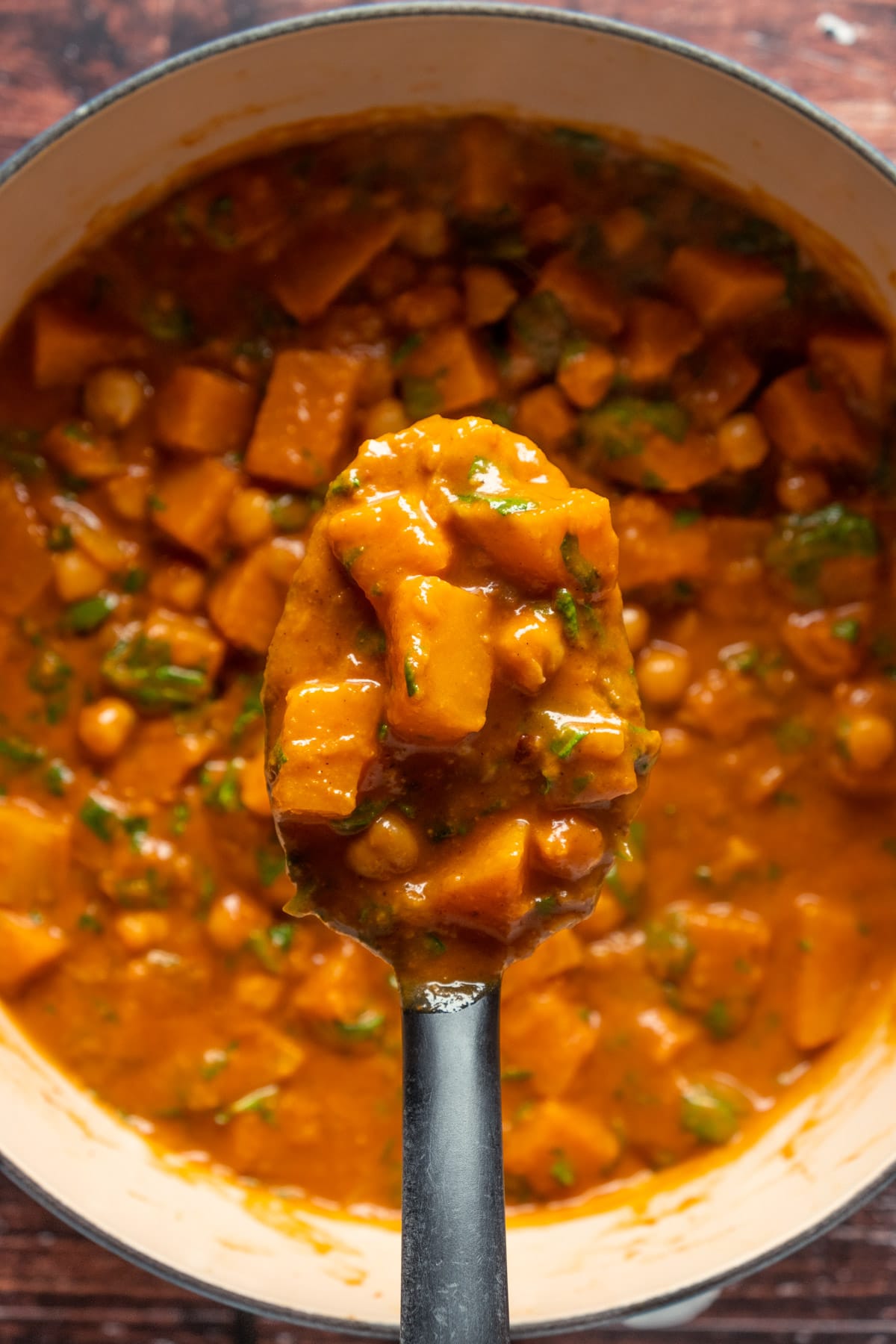 Cooked butternut squash curry in a ceramic pot with a black serving spoon.