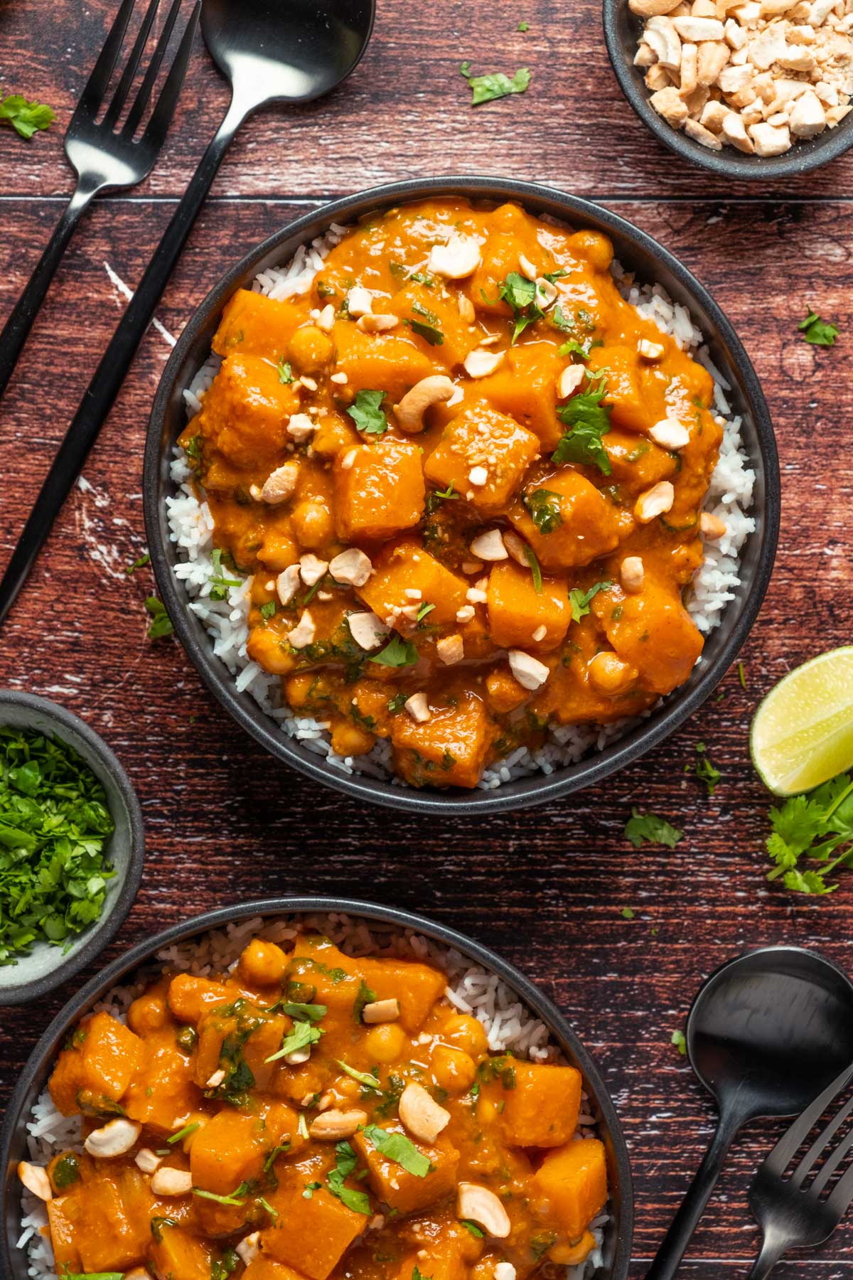 Veganes Butternusskürbis-Curry mit Reis in schwarzen Schalen.