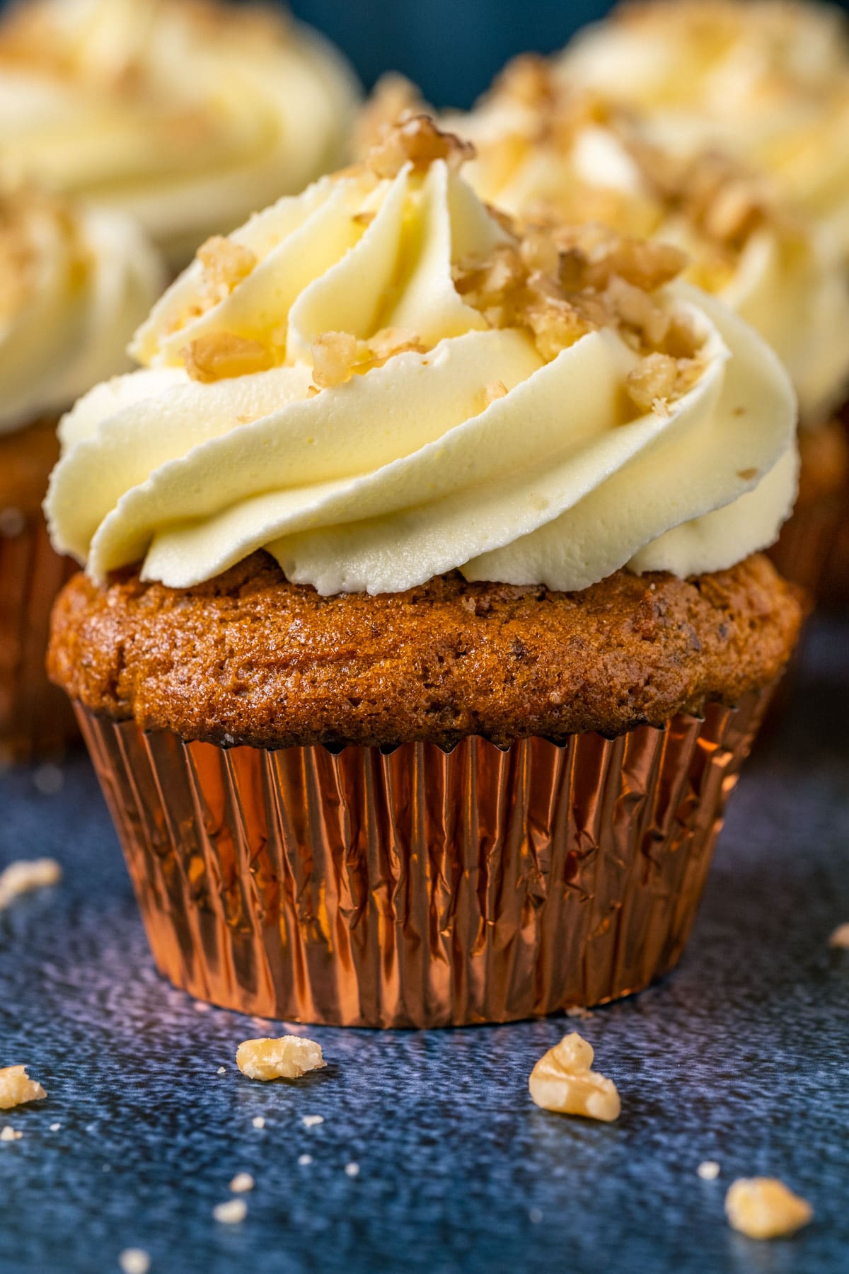 Gluten free carrot cake cupcakes topped with frosting and chopped walnuts.