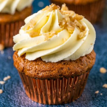 Vegan gluten free carrot cake cupcake topped with frosting and chopped walnuts.