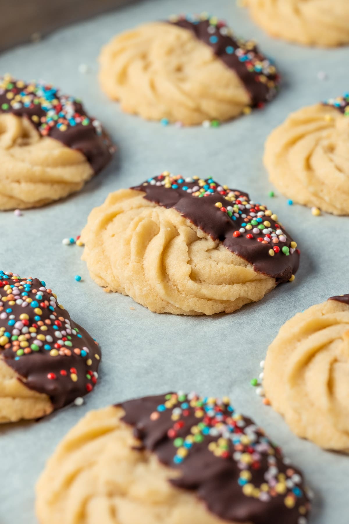 Butter cookies dipped in chocolate and topped with sprinkles on a parchment lined baking tray.