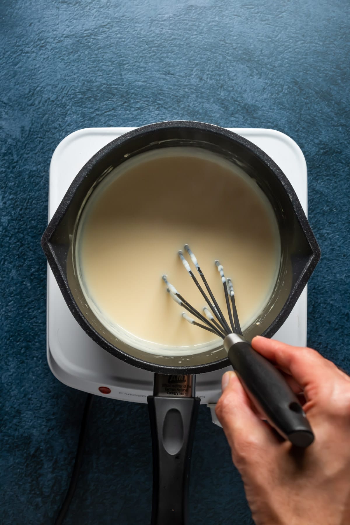Vegan white sauce in a saucepan with a whisk.