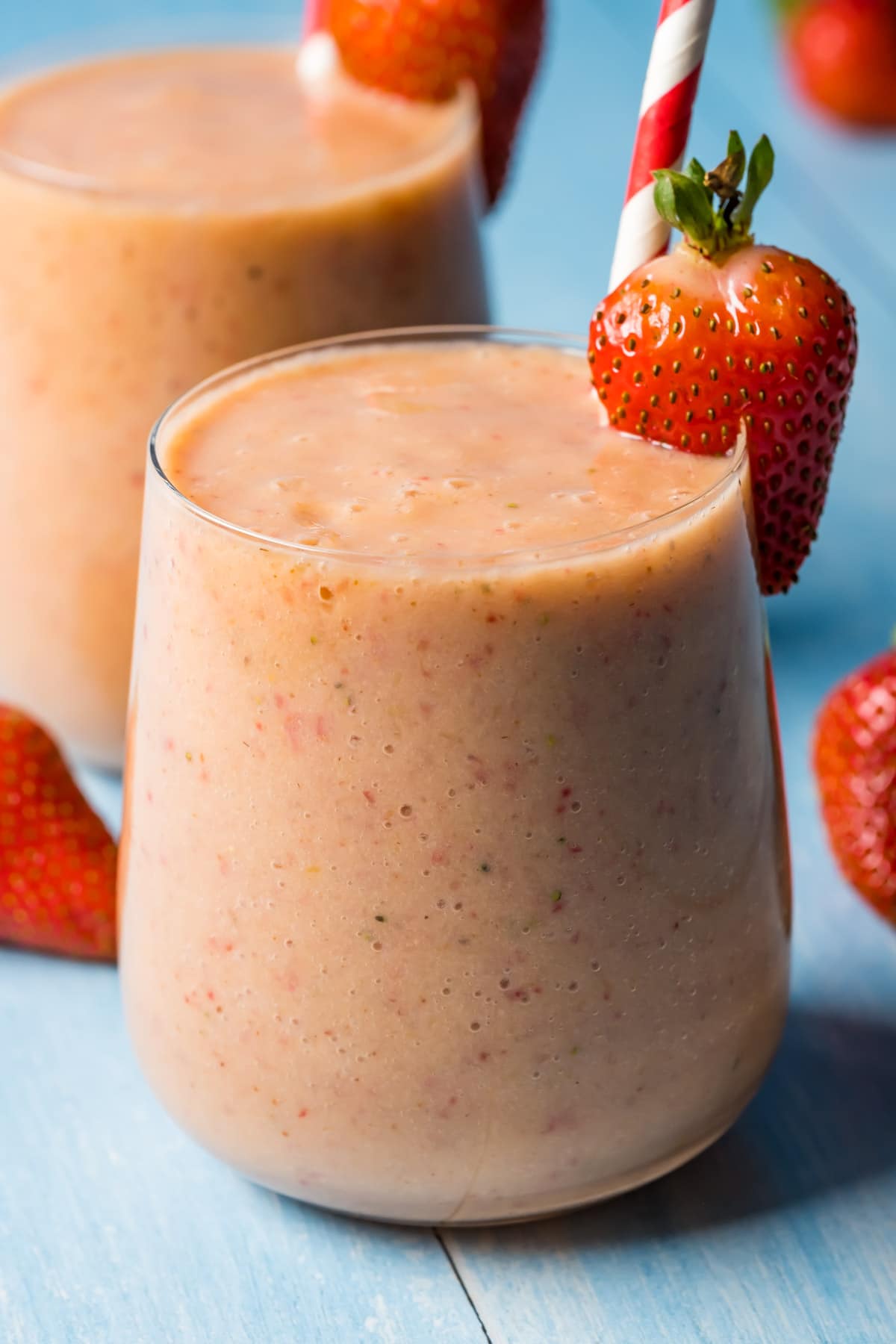 Strawberry mango smoothie in glasses with striped straws.
