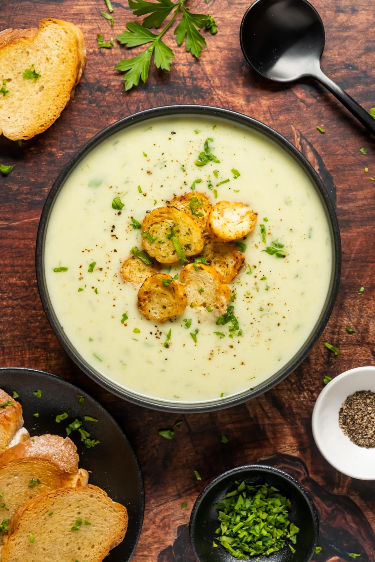 Vegan celery soup topped with chopped parsley and croutons in a black bowl. 