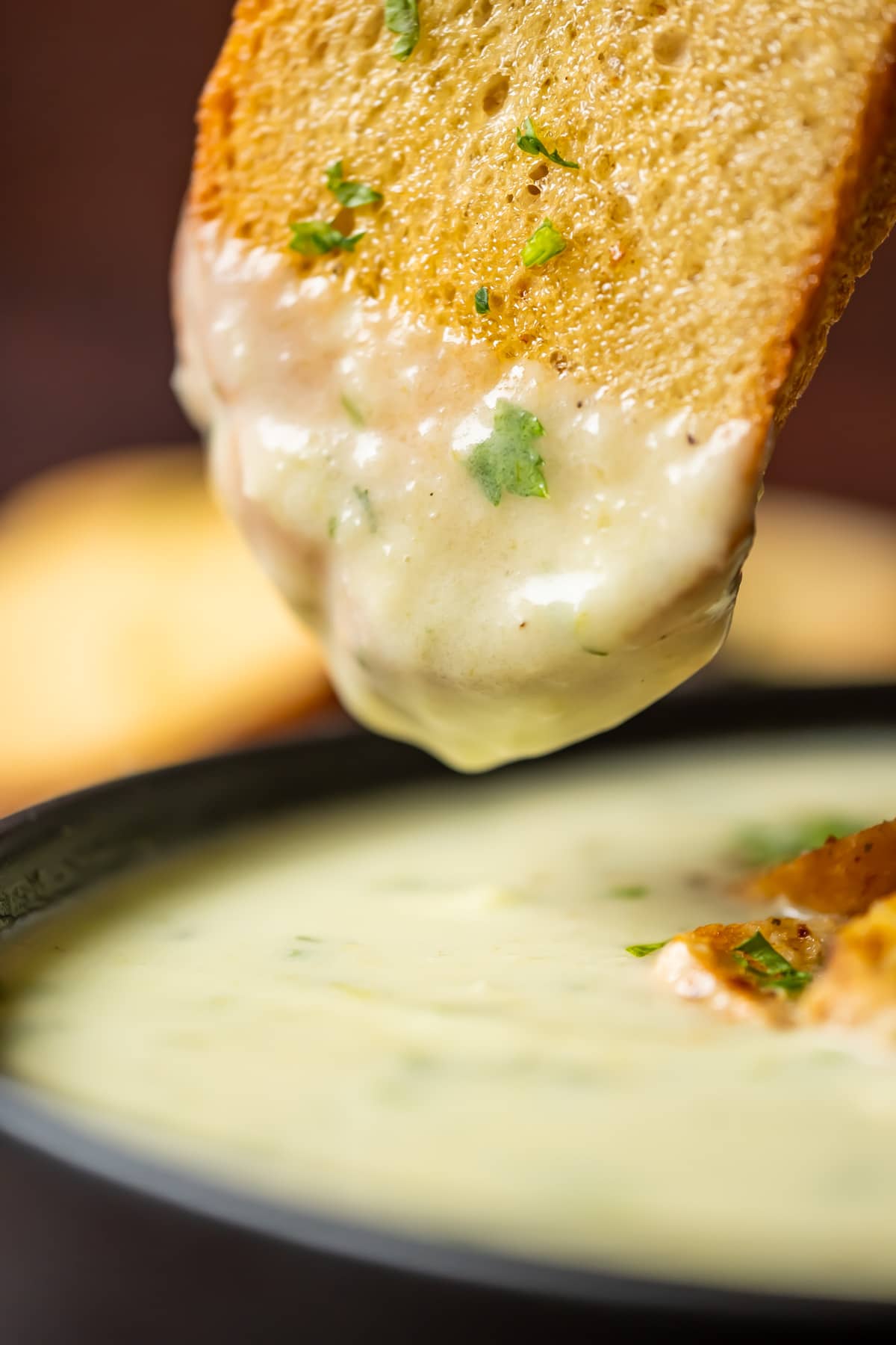 Slice of toasted bread dipping into celery soup.