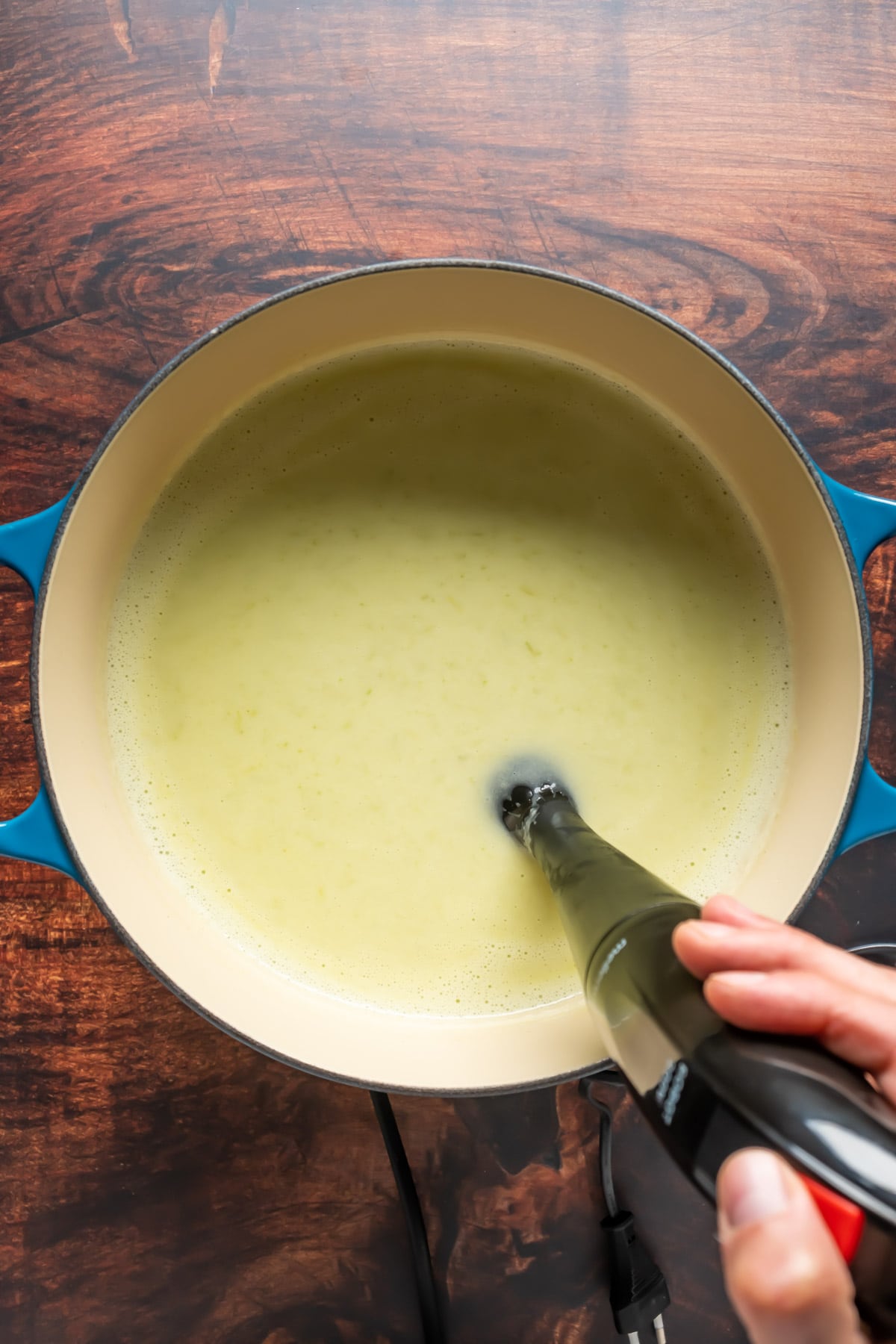Vegan celery soup in a pot with an immersion blender.