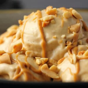 Scoops of banana nice cream topped with drizzled peanut butter and peanuts in a bowl.