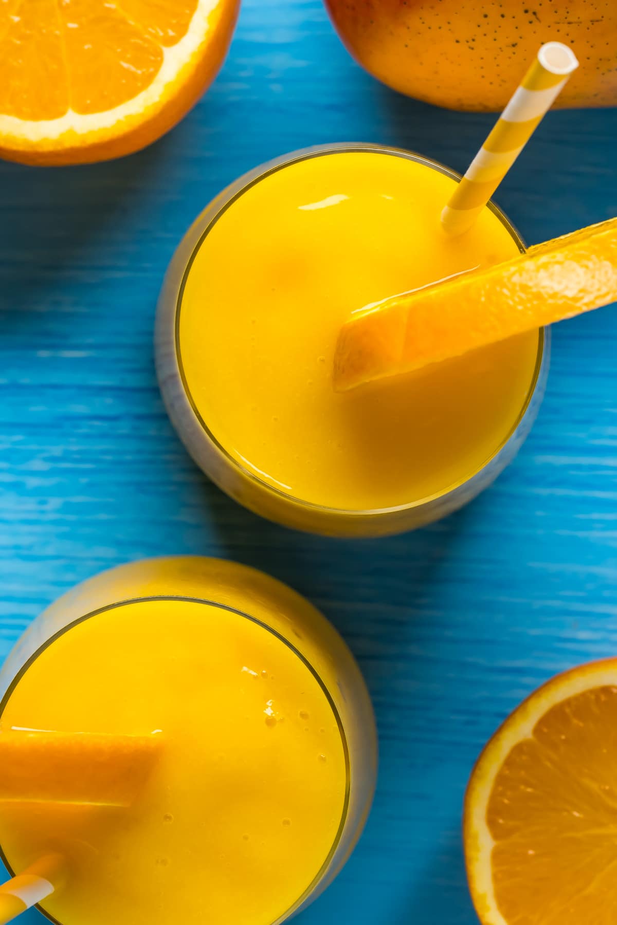 Mango orange smoothie in glasses with a slice of fresh orange and straws. 