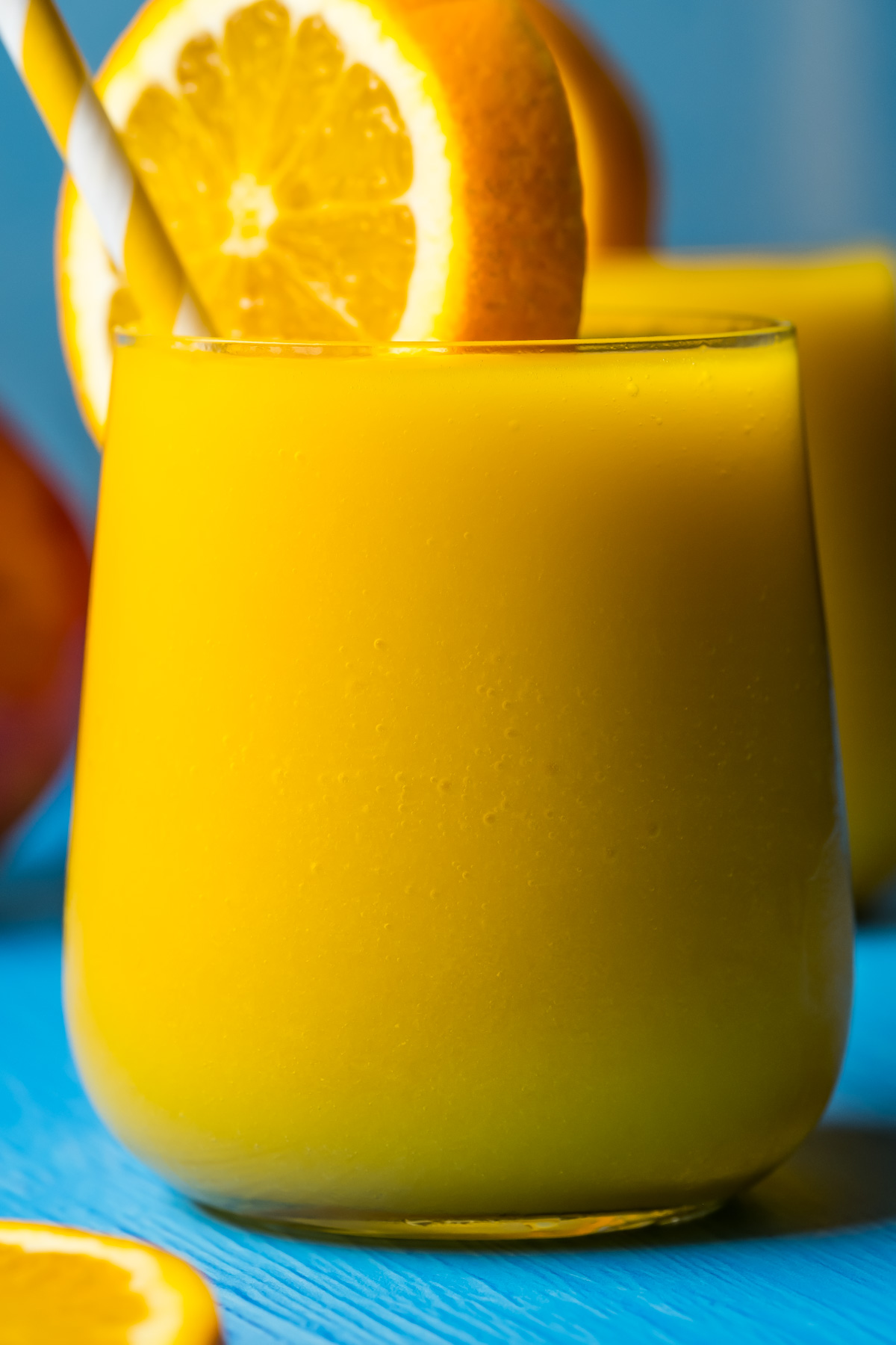 Mango orange smoothie in glasses with a slice of fresh orange and straws.
