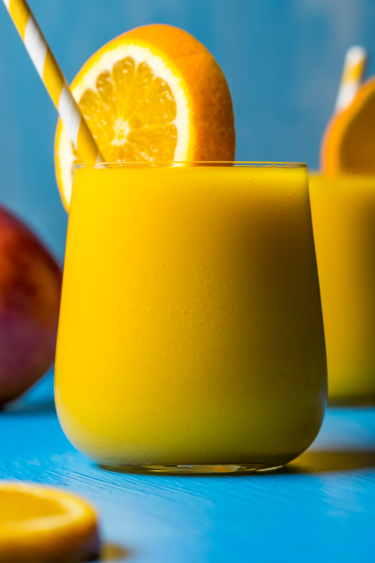 Mango orange smoothie in glasses with a slice of fresh orange and straws.