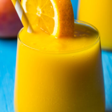 Mango orange smoothie in a glass with a fresh orange slice and a straw.
