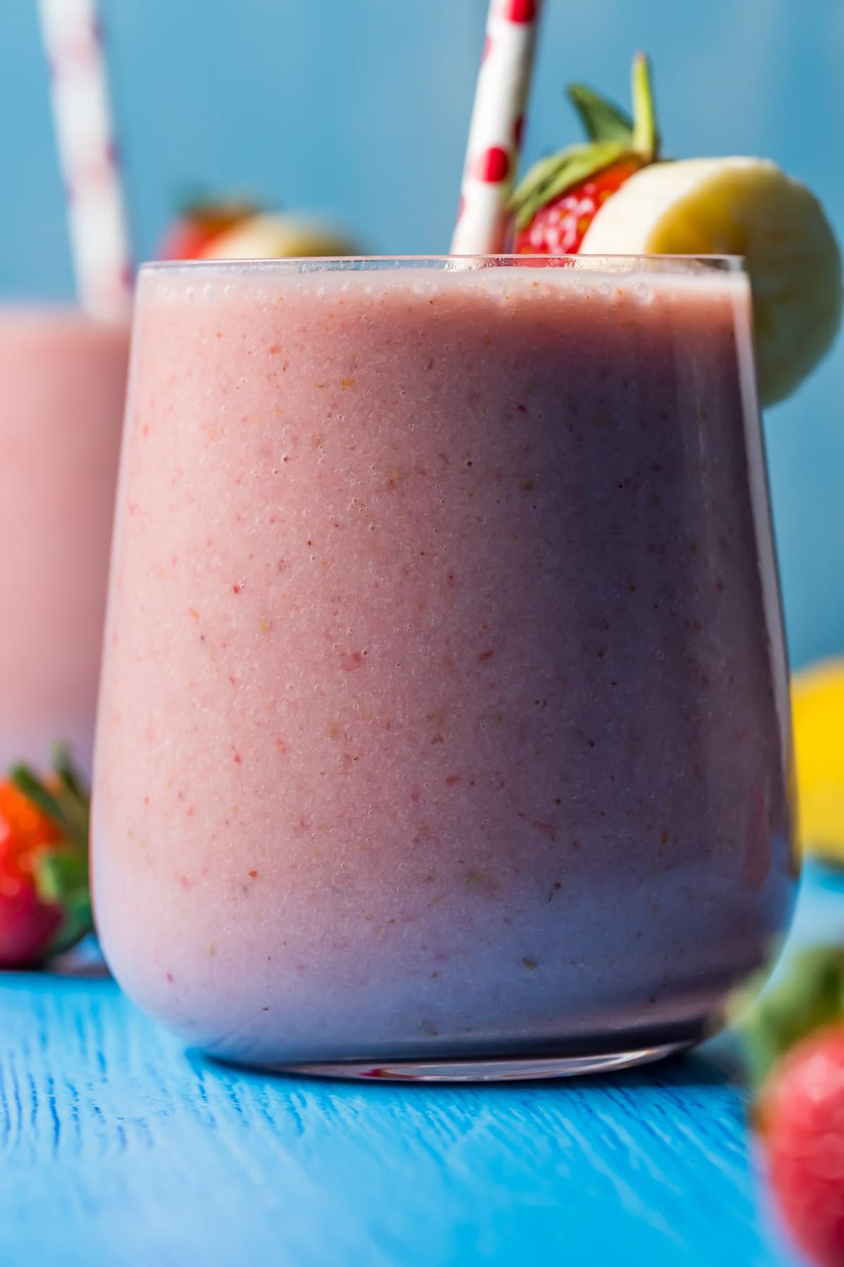 Strawberry banana smoothie in glasses with stripey straws.