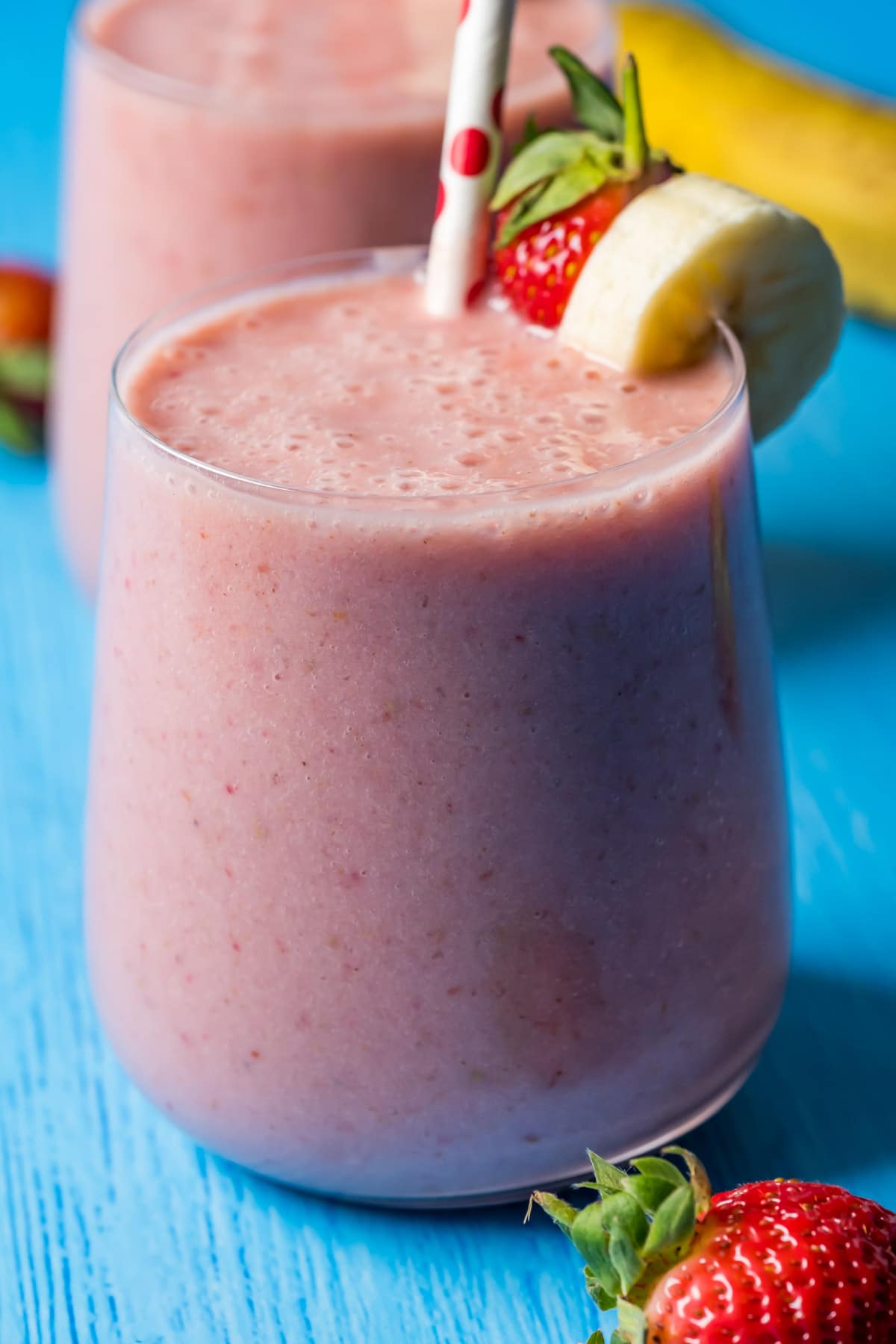 Strawberry banana smoothie in glasses with stripey straws.