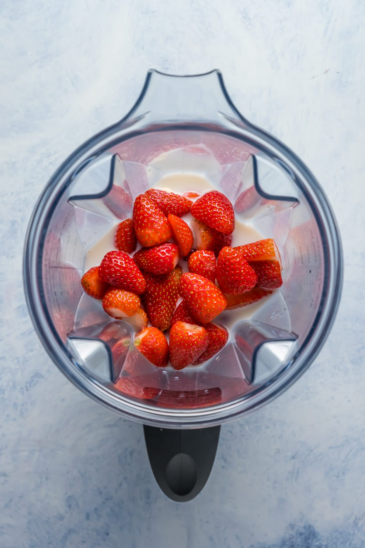Ingredients for strawberry smoothie in a blender jug.