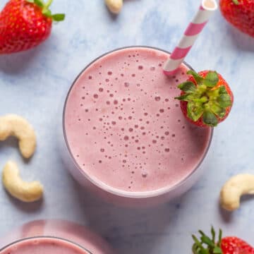 Strawberry smoothie in a glass with a striped straw.