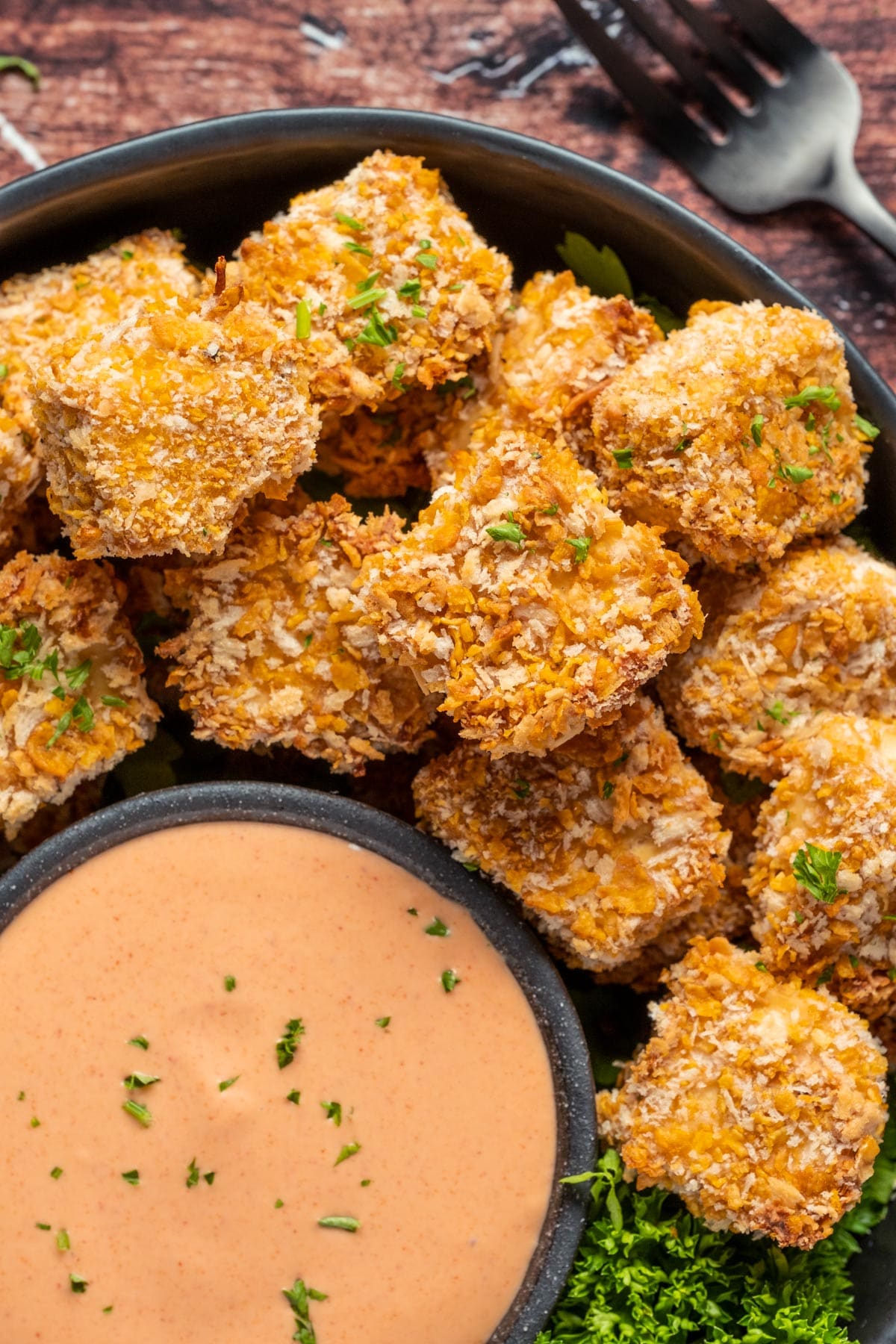 Vegan chicken nuggets stacked up on a plate with a bowl of yum yum sauce. 