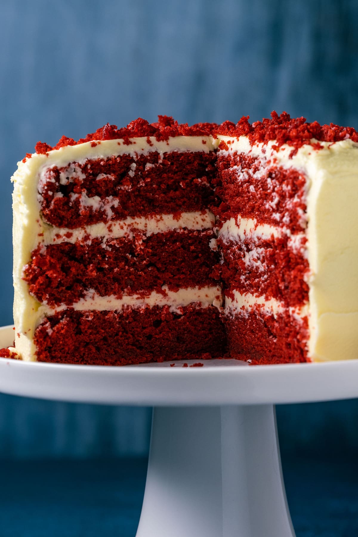 Vegan red velvet cake with slices missing, on a white cake stand.