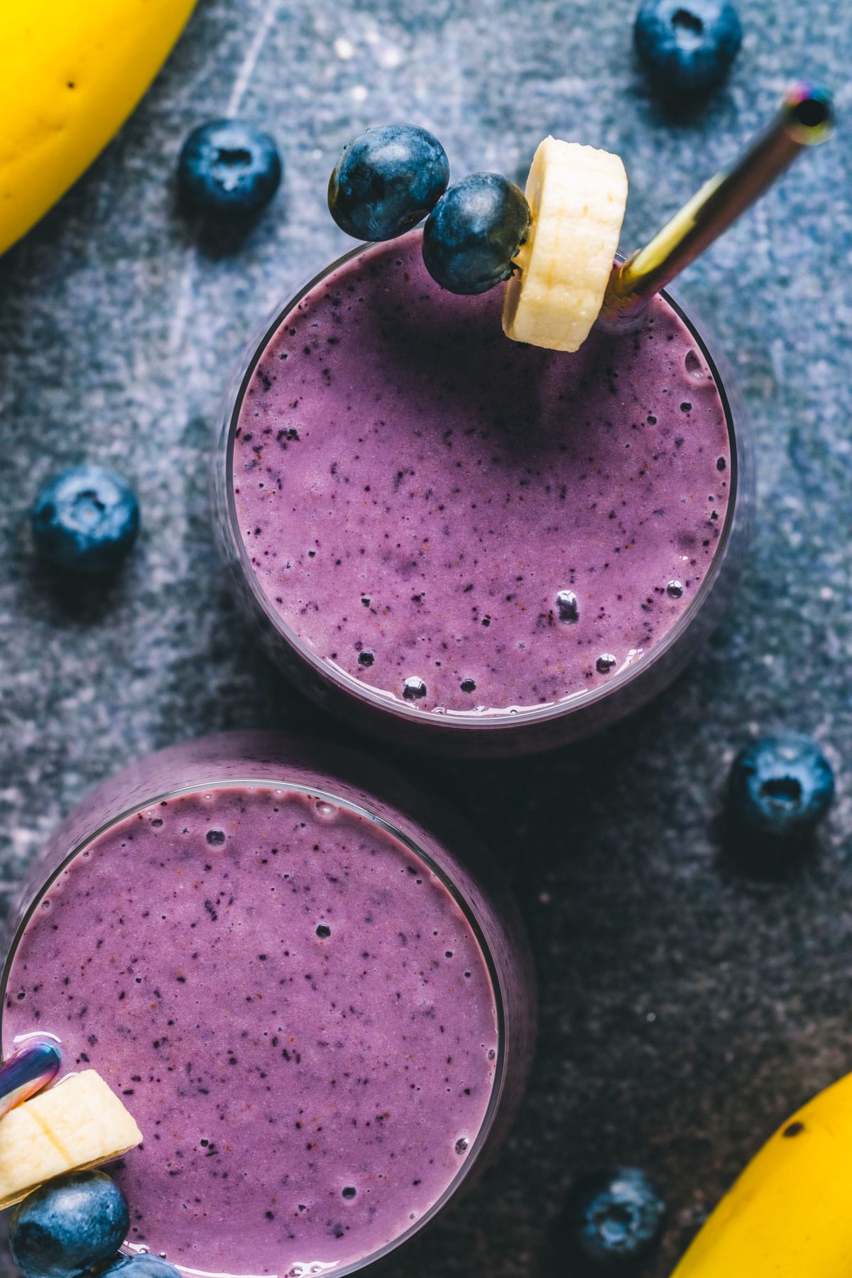 Blueberry banana smoothie in two glasses with straws. 