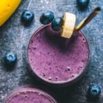 Blueberry banana smoothie in a glass with a straw.