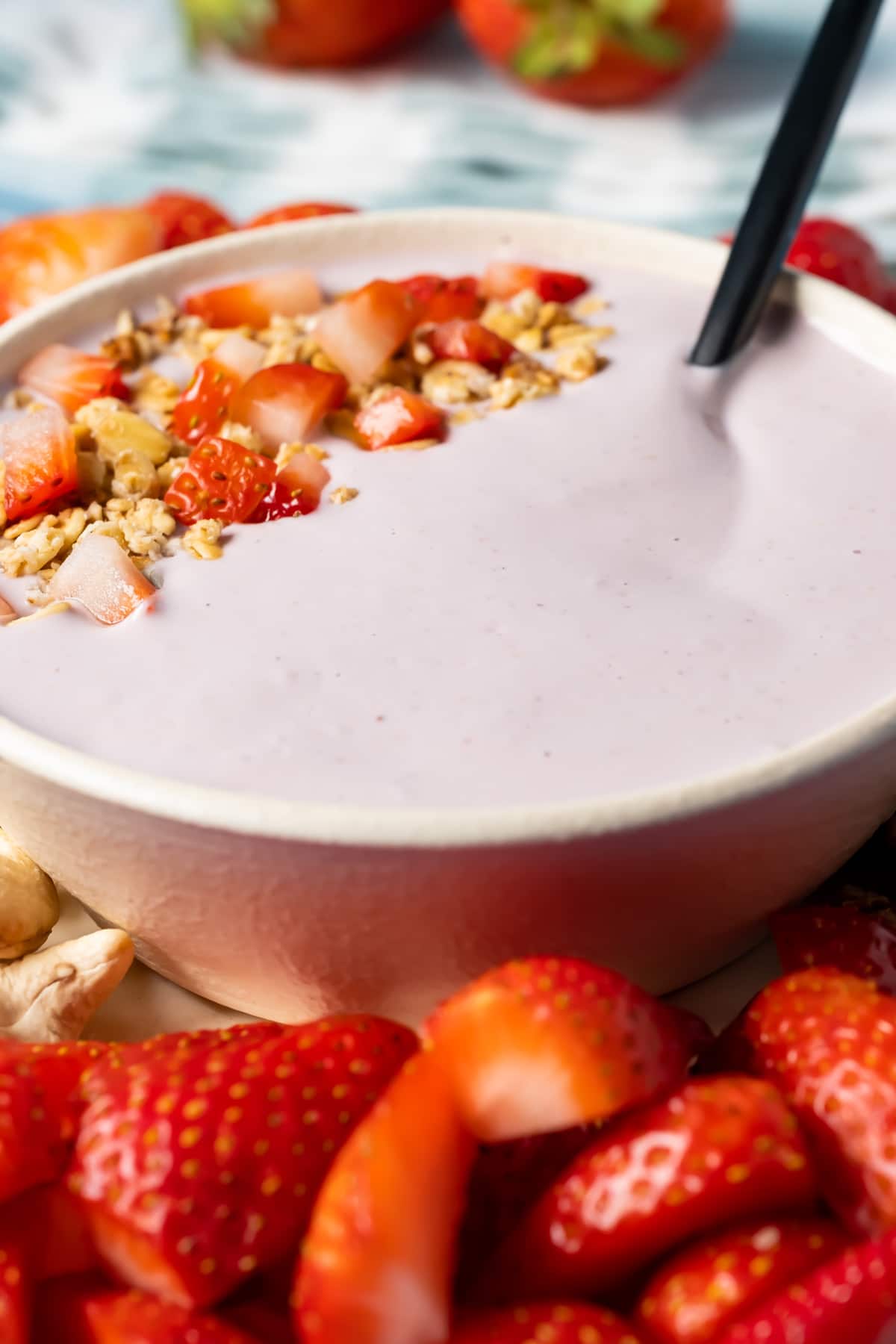 Vegan yogurt topped with granola and sliced strawberries in a bowl with a spoon.
