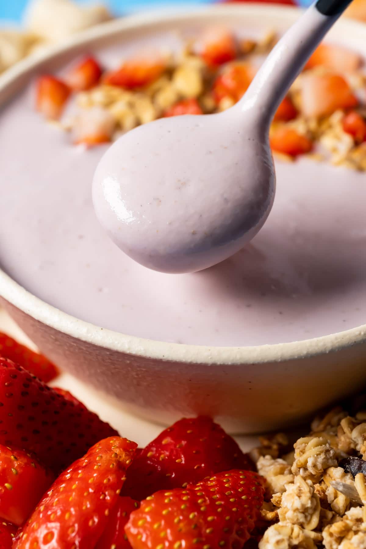 Vegan yogurt topped with granola and sliced strawberries in a bowl with a spoon.