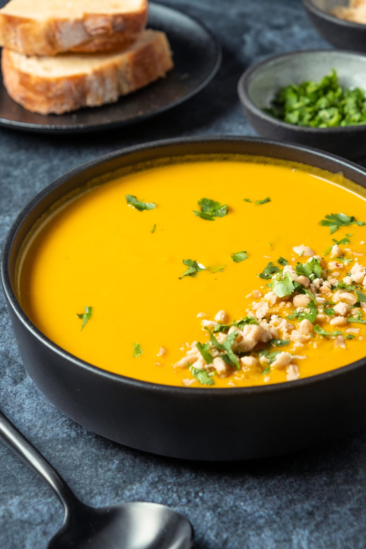 Vegan carrot soup in a black bowl with fresh chopped cilantro and crushed peanuts. 