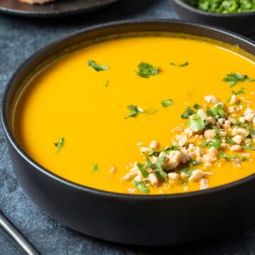 Vegan carrot soup in a black bowl with fresh chopped cilantro and crushed peanuts.
