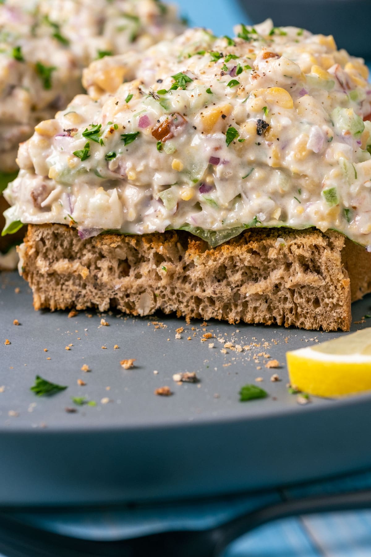 Open faced sandwich topped with vegan chicken salad and sliced in half on a gray plate.