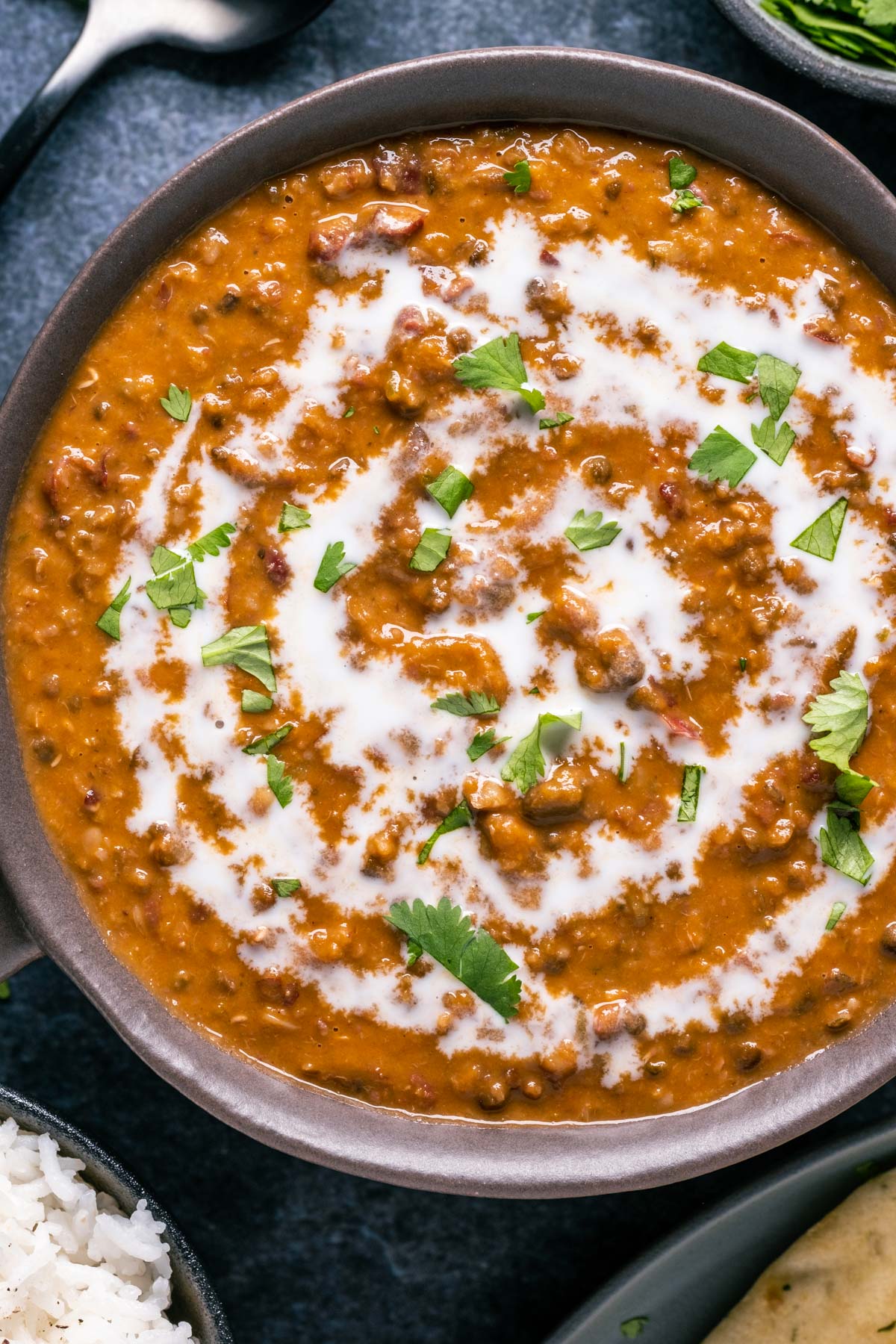 Vegan dal makhani topped with a drizzle of coconut cream and fresh chopped cilantro in a brown bowl. 