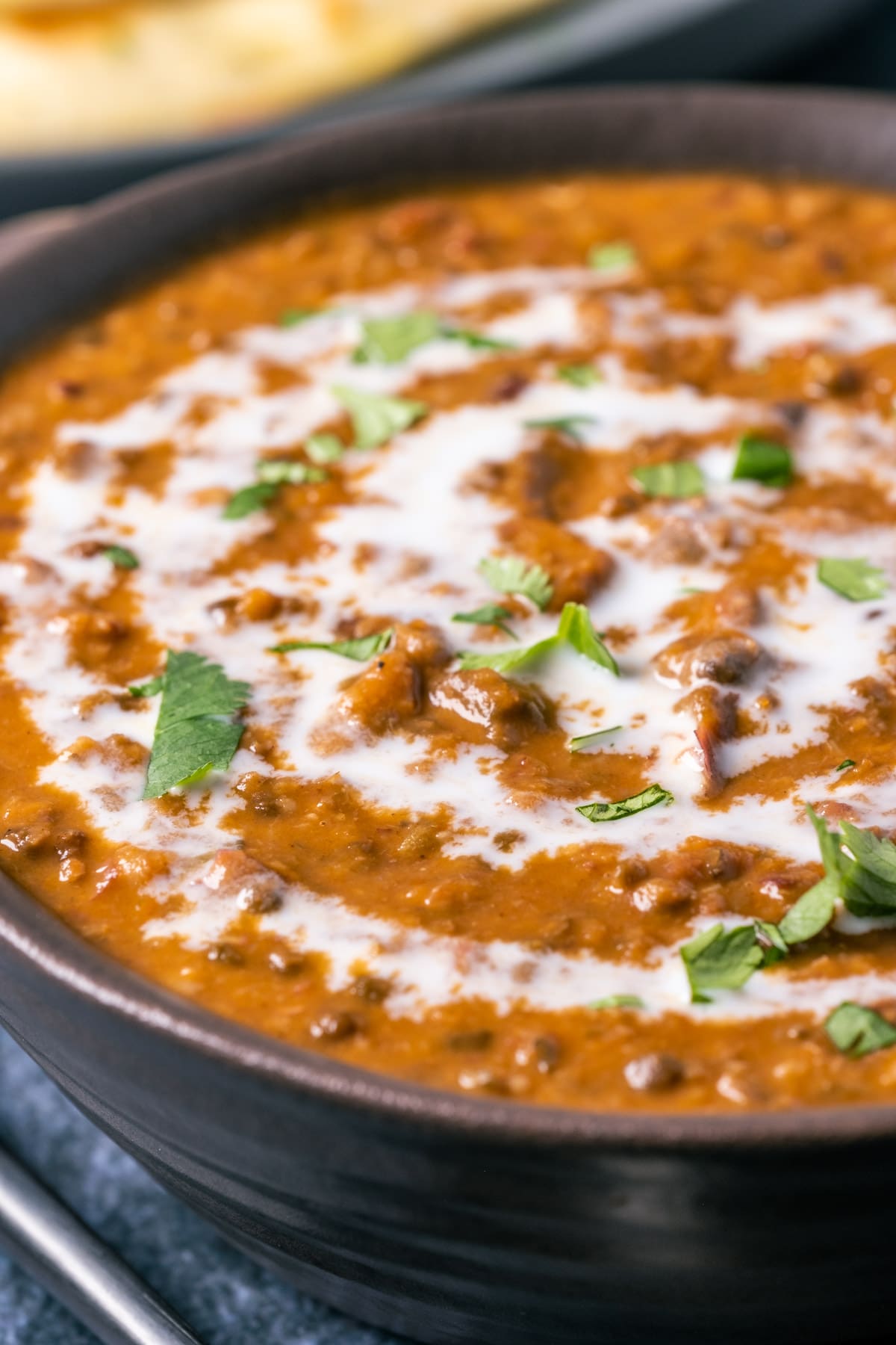 Vegan dal makhani topped with a drizzle of coconut cream and fresh chopped cilantro in a brown bowl.
