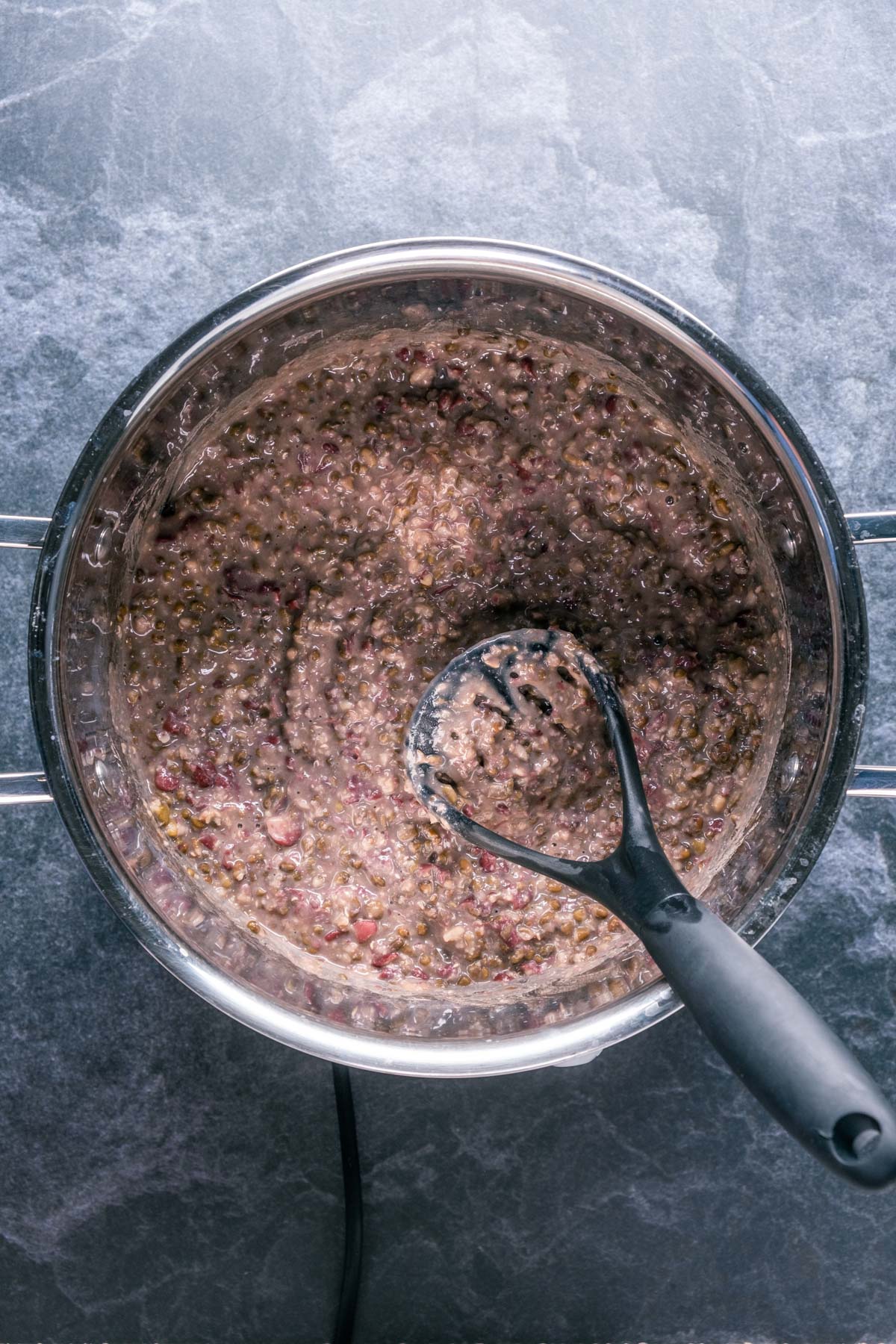 Mashing cooked urad dal and kidney beans in a pot with a potato masher.
