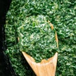 Vegan creamed spinach in a skillet with a wooden spoon.