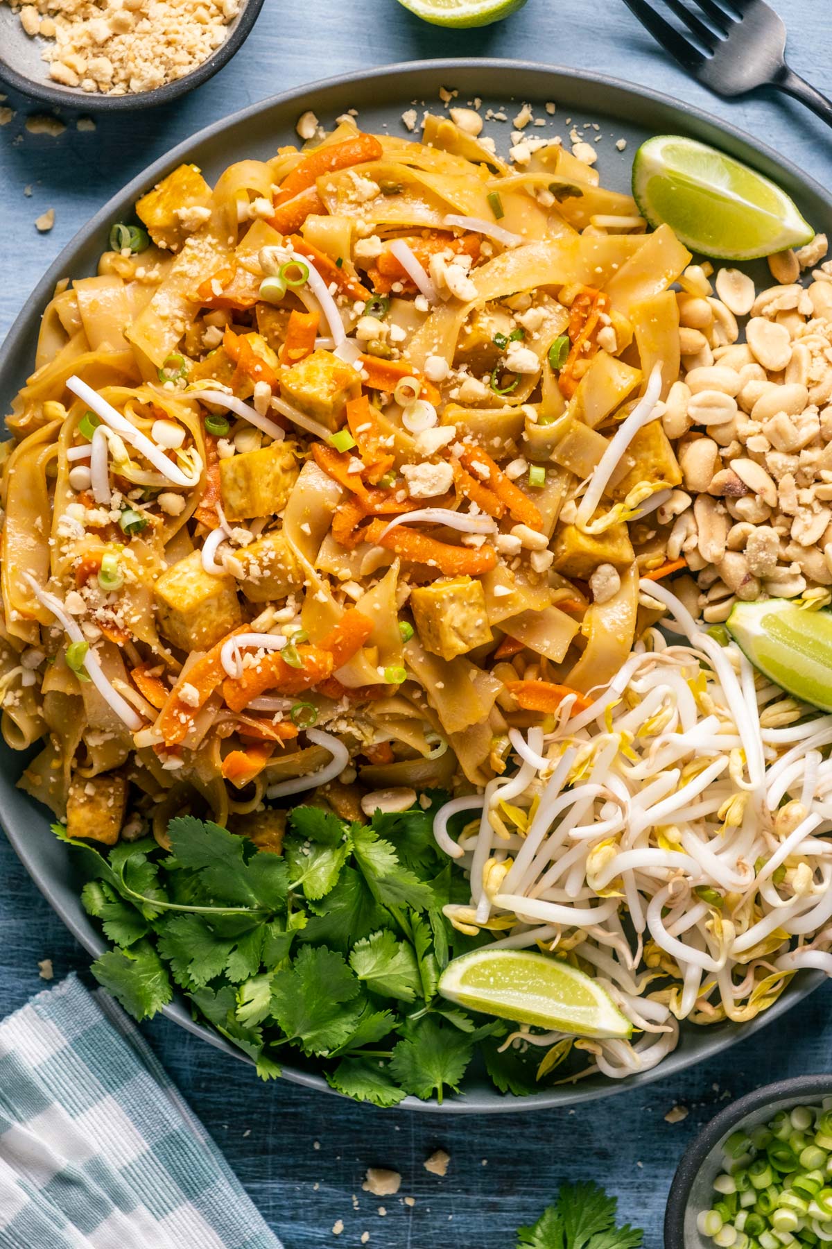 Vegan pad thai on a gray plate with bean sprouts, peanuts, lime wedges and cilantro. 