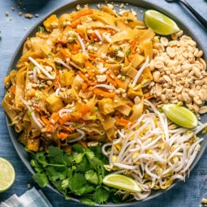 Vegan pad thai on a gray plate with bean sprouts, peanuts, lime wedges and cilantro.