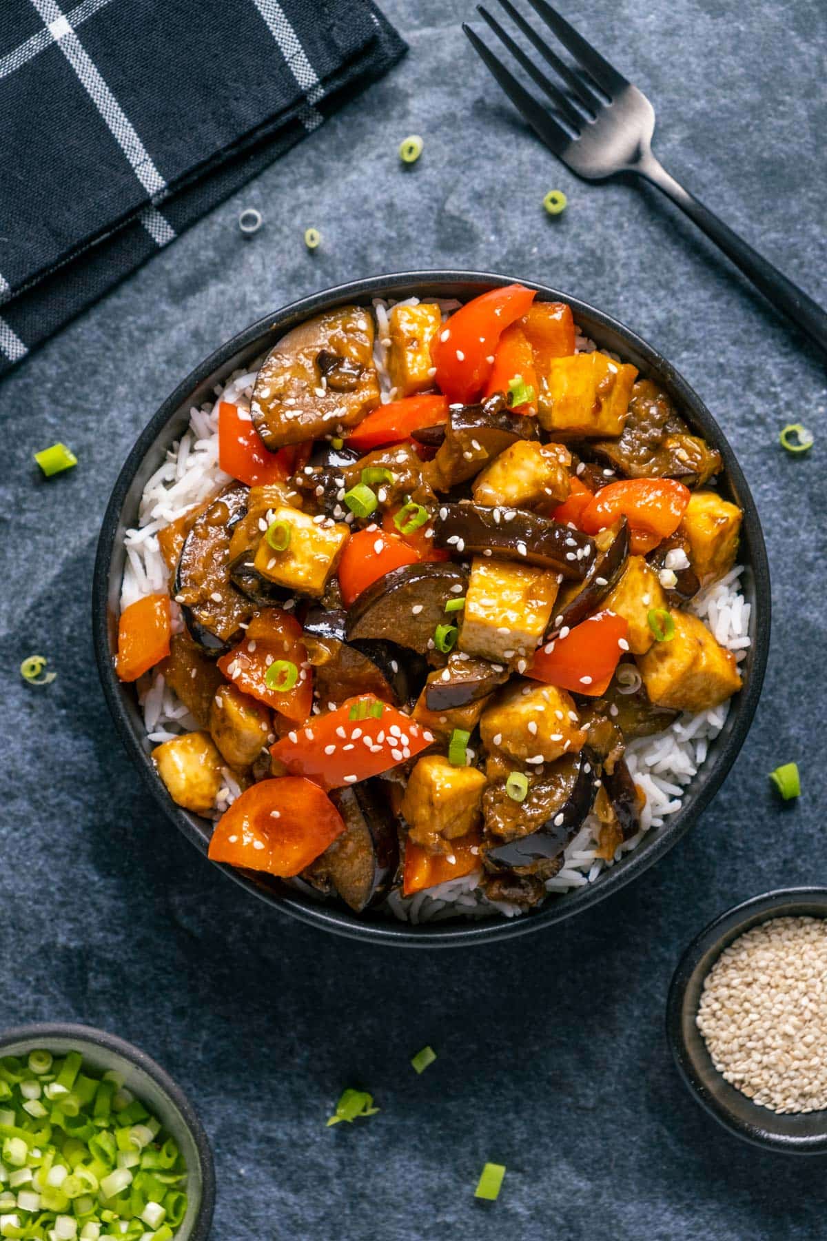Eggplant tofu stir fry with rice in a black bowl. 