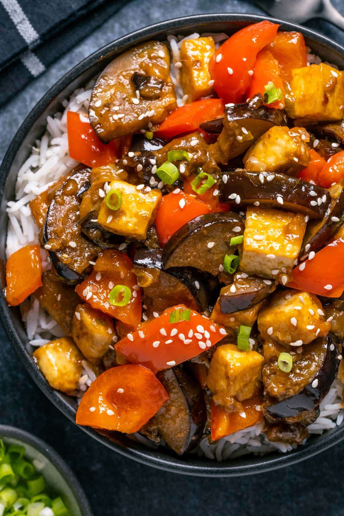 Eggplant tofu stir fry with rice in a black bowl.