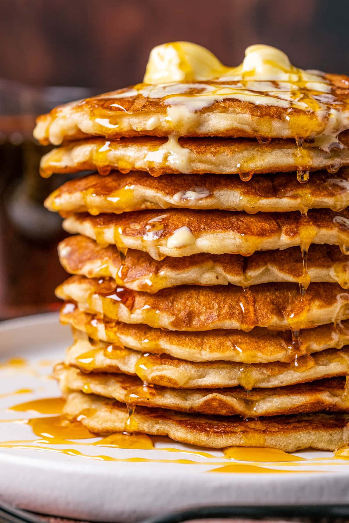 Stack of vegan oatmeal pancakes topped with vegan butter and syrup on a white plate.