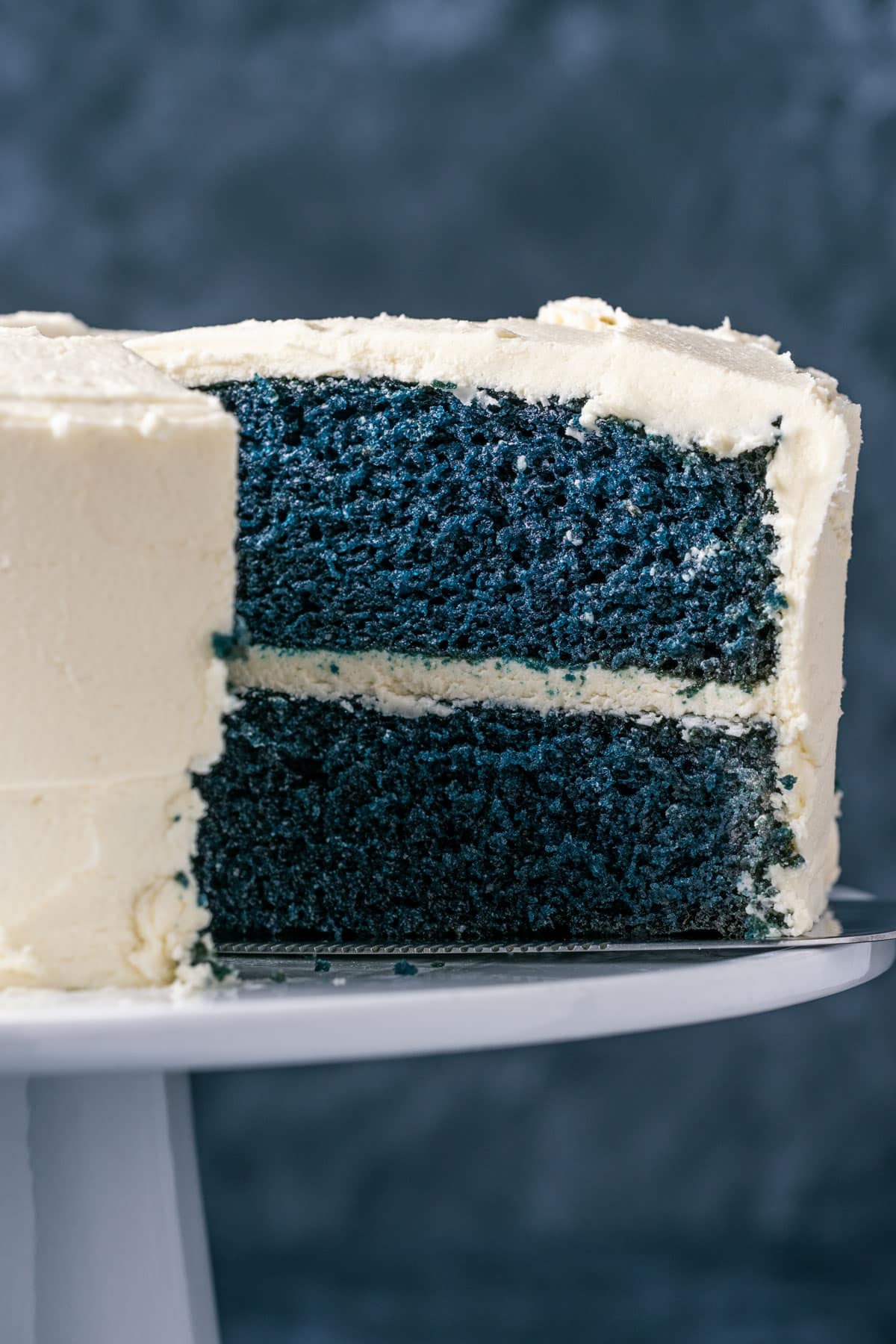 Sliced blue velvet cake on a white cake stand.