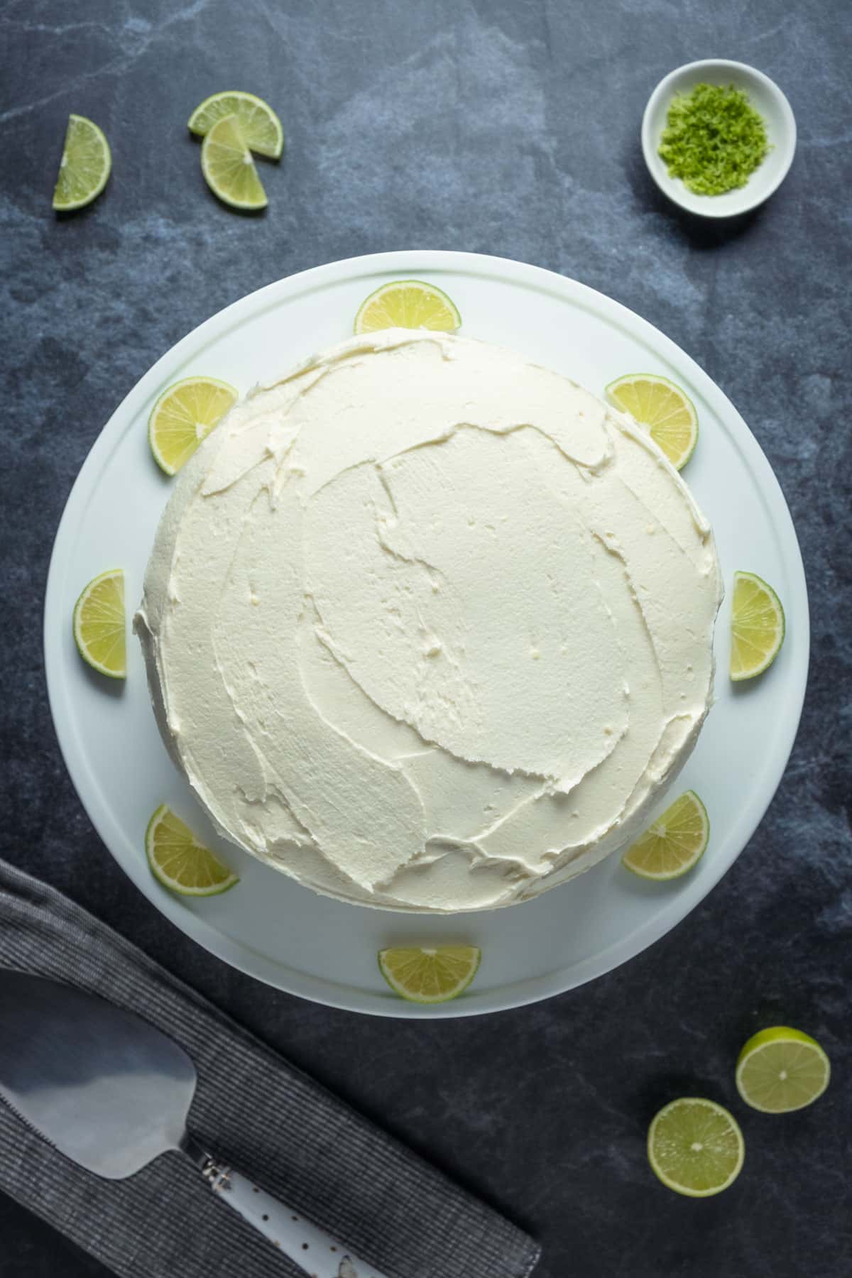 Frosted key lime cake on a white cake stand.