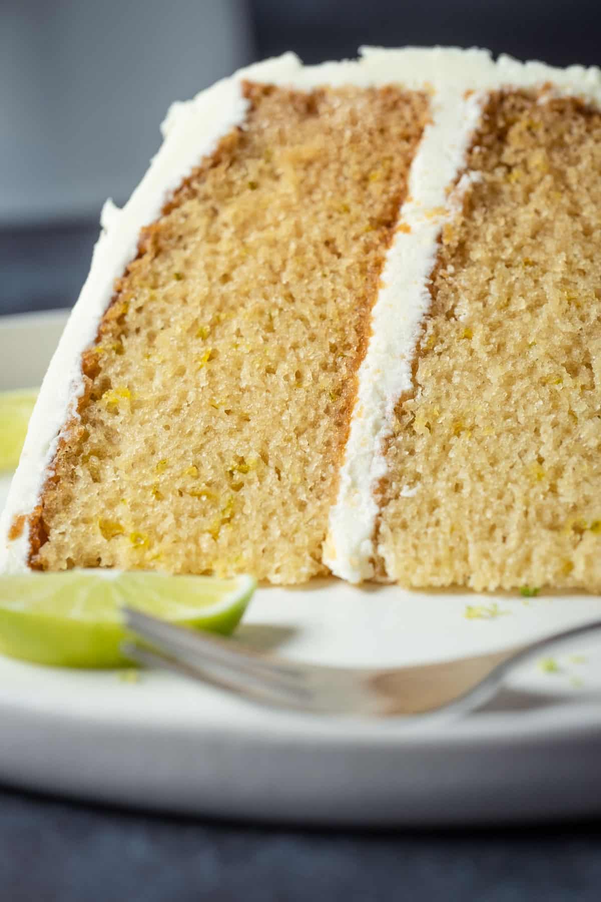 Slice of vegan key lime cake on a white plate with a cake fork.