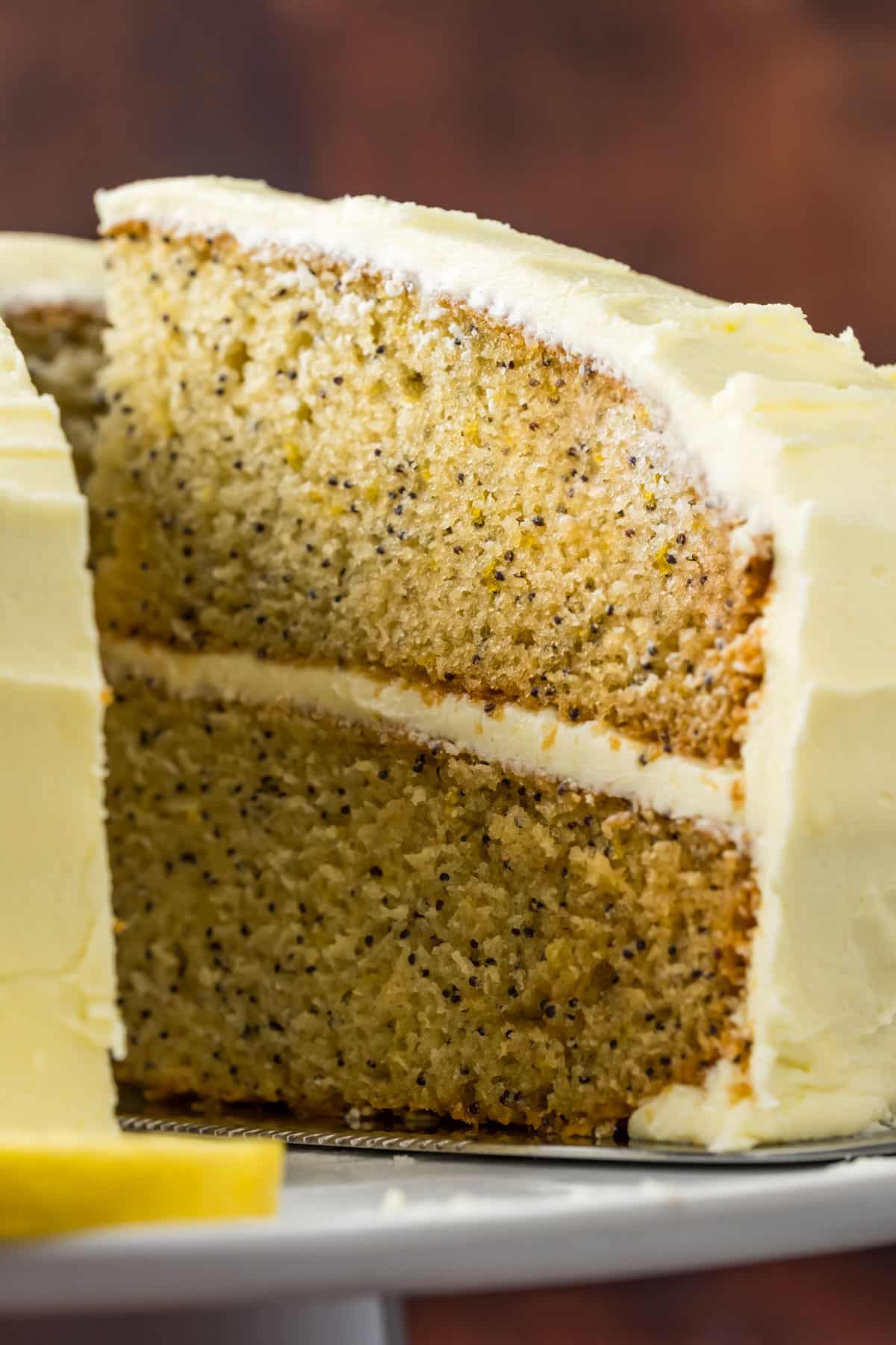 Sliced vegan lemon poppy seed cake on a white cake stand.