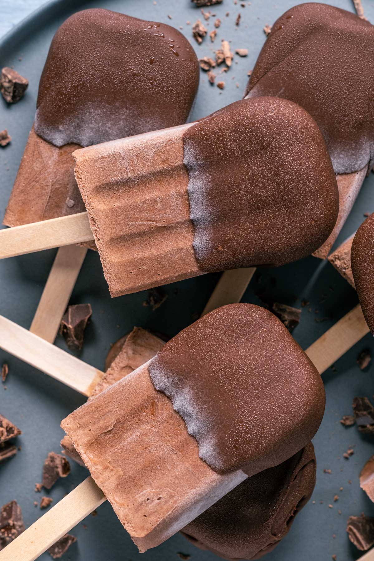 Chocolate dipped popsicles stacked up on a plate.