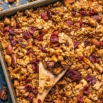 Vegan granola on a baking sheet with a wooden spoon.