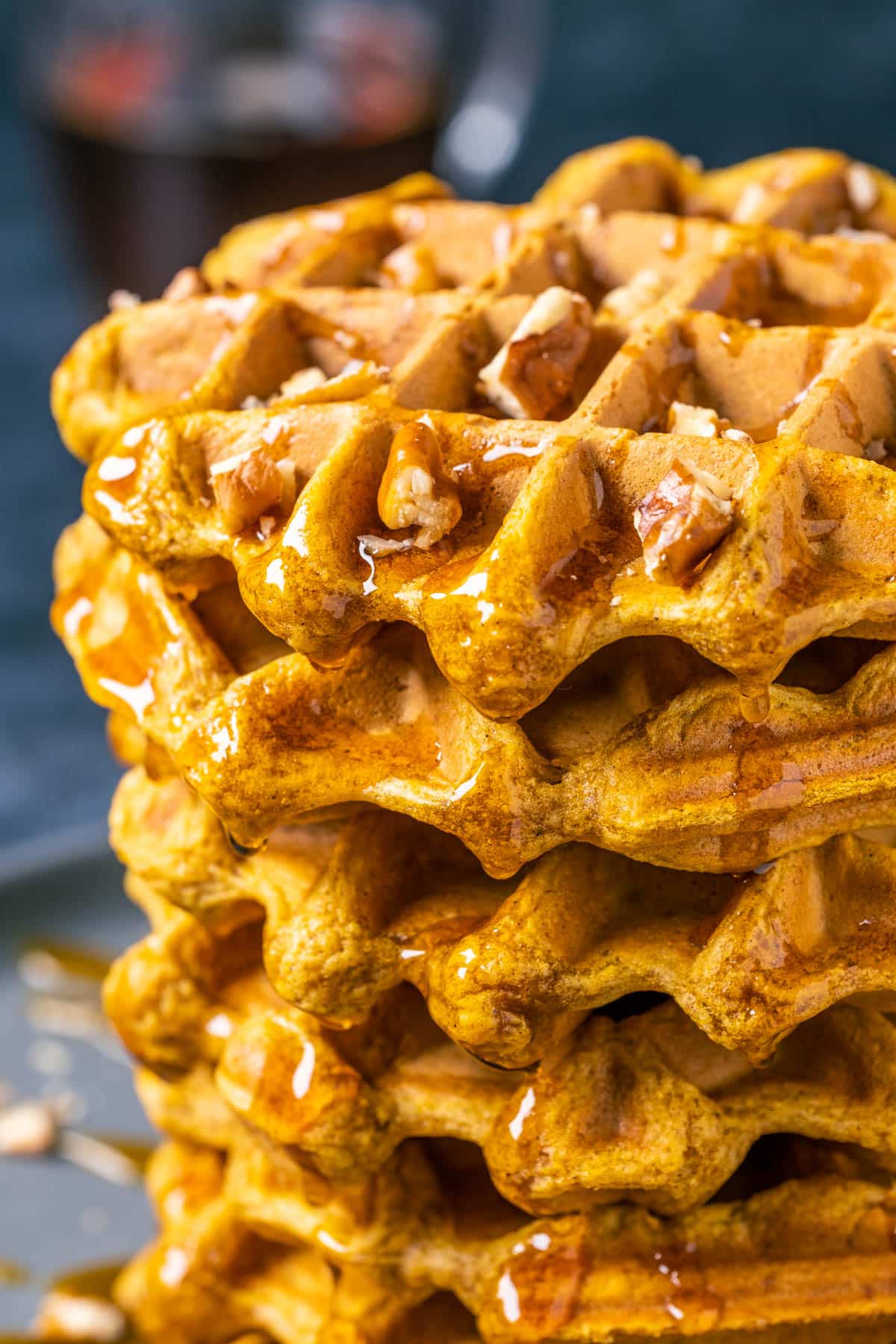 Stack of vegan pumpkin waffles with syrup and pecans.